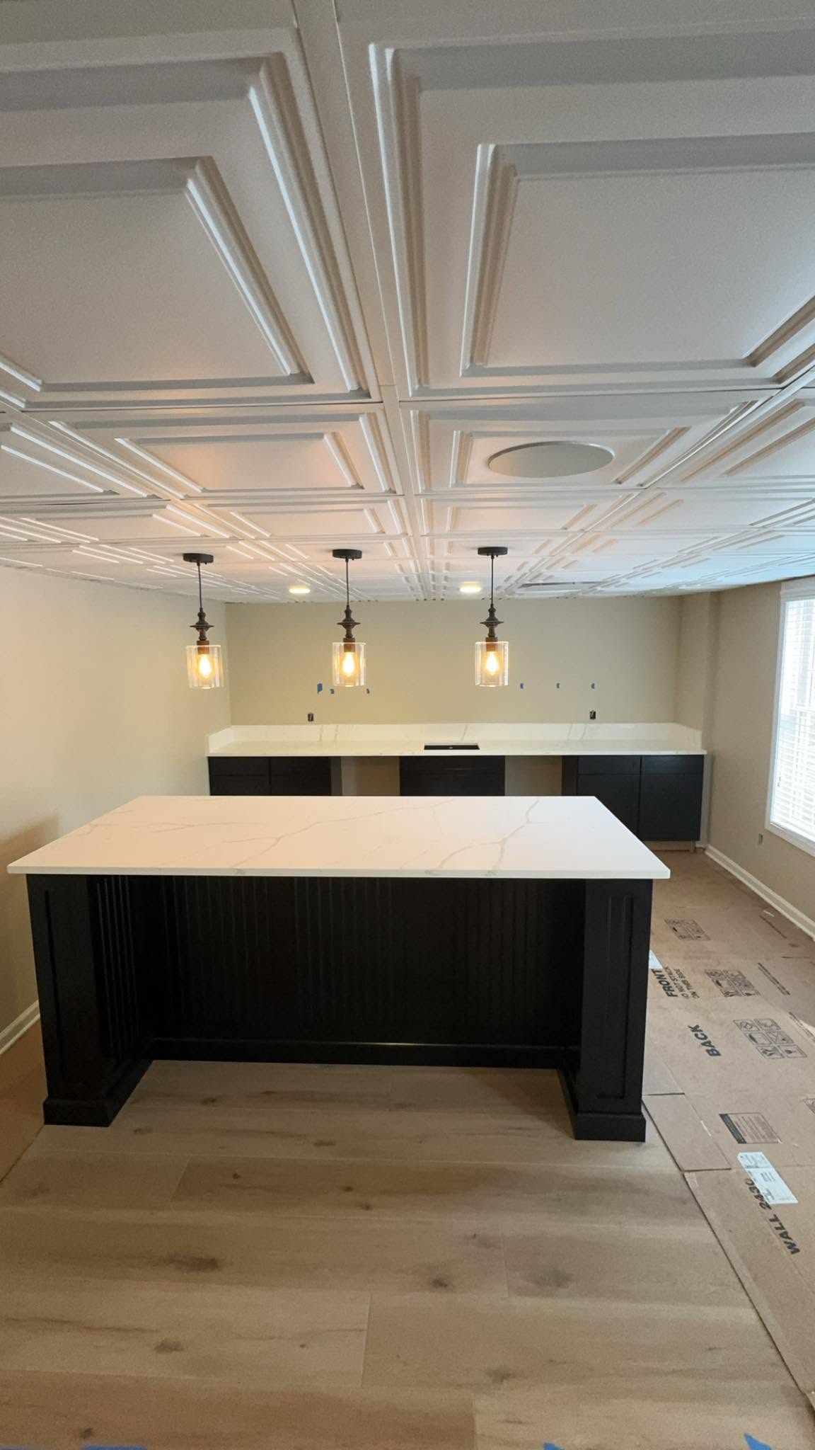 Calacatta quartz island on a black beadboard base under glass pendants, with a matching back bar