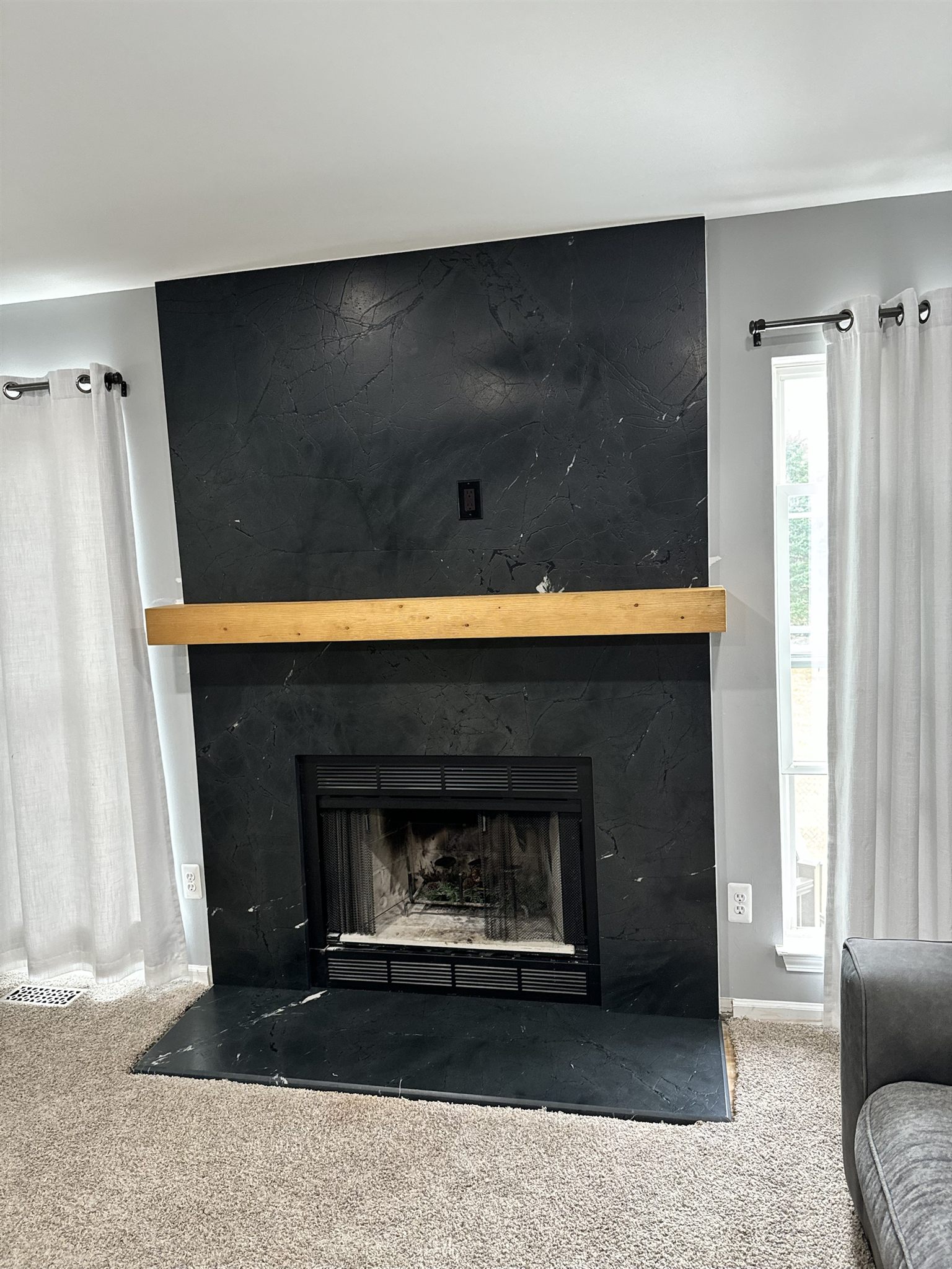 Floor-to-ceiling black stone fireplace surround with white veining, a matching hearth and a natural wood mantel
