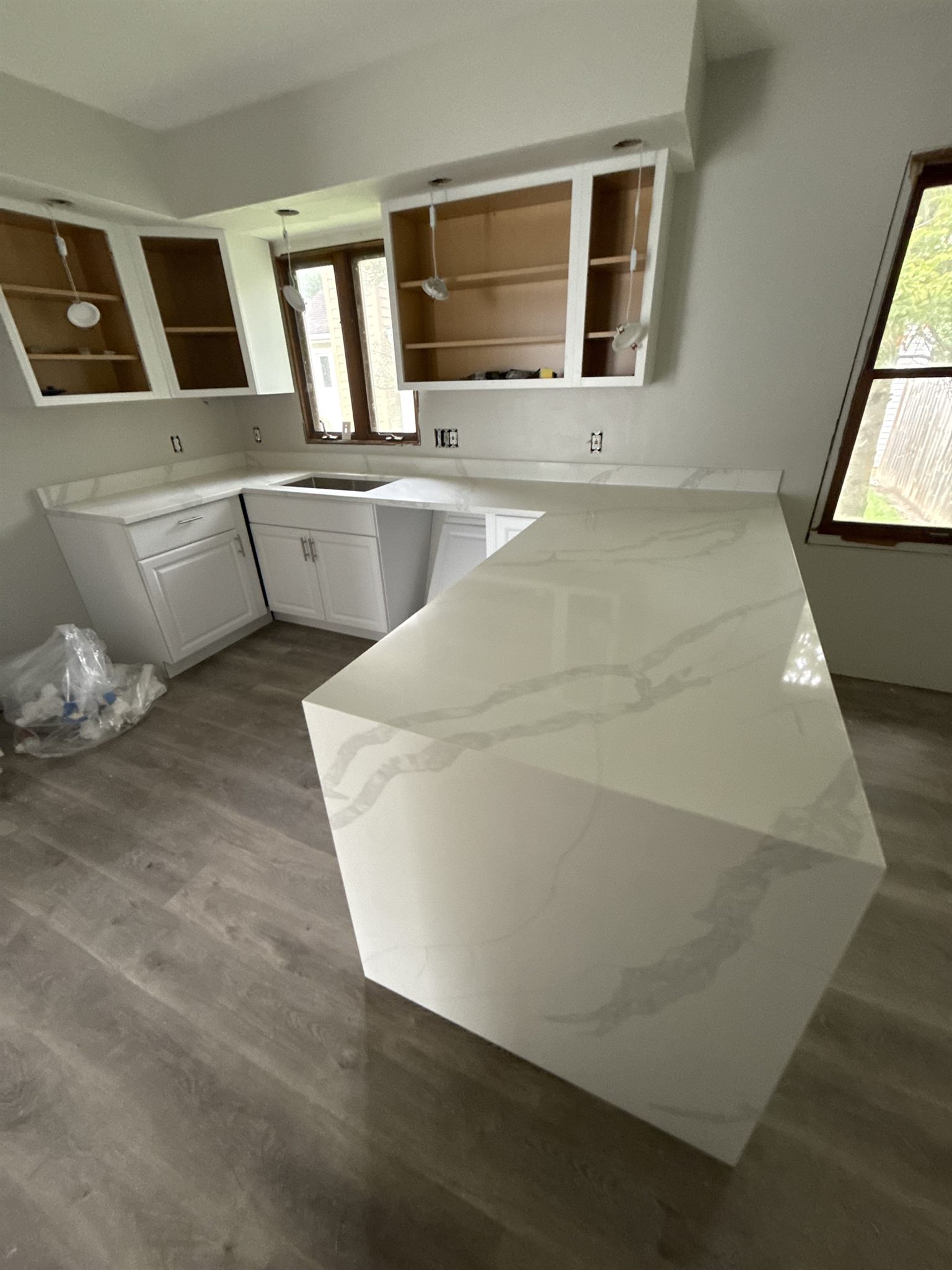 L-shaped Calacatta quartz peninsula with a mitered waterfall end, bold grey veins running across the top and down the side panel