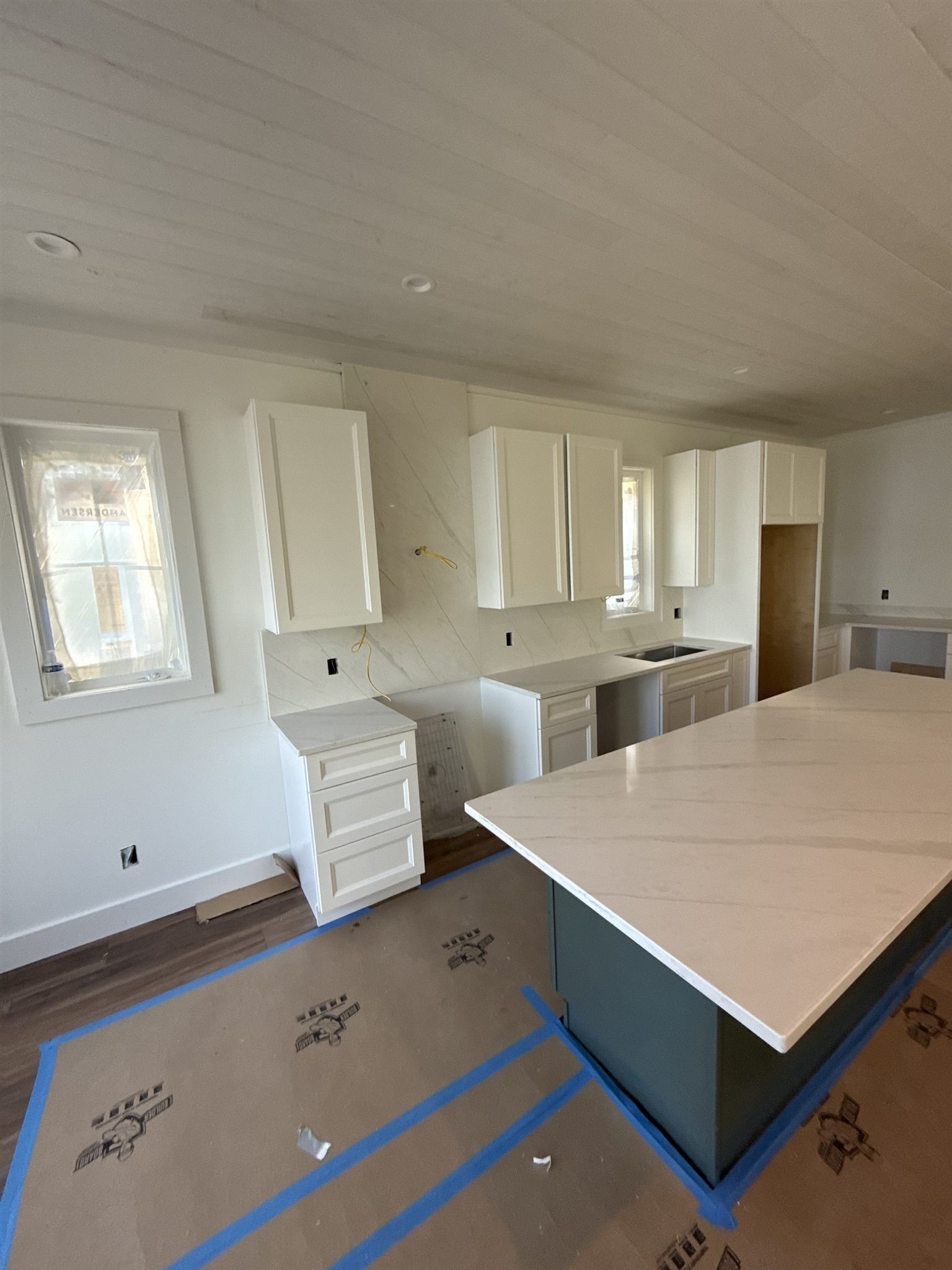 White kitchen with a quartz island over dark green cabinets and a full-height slab backsplash with diagonal veining