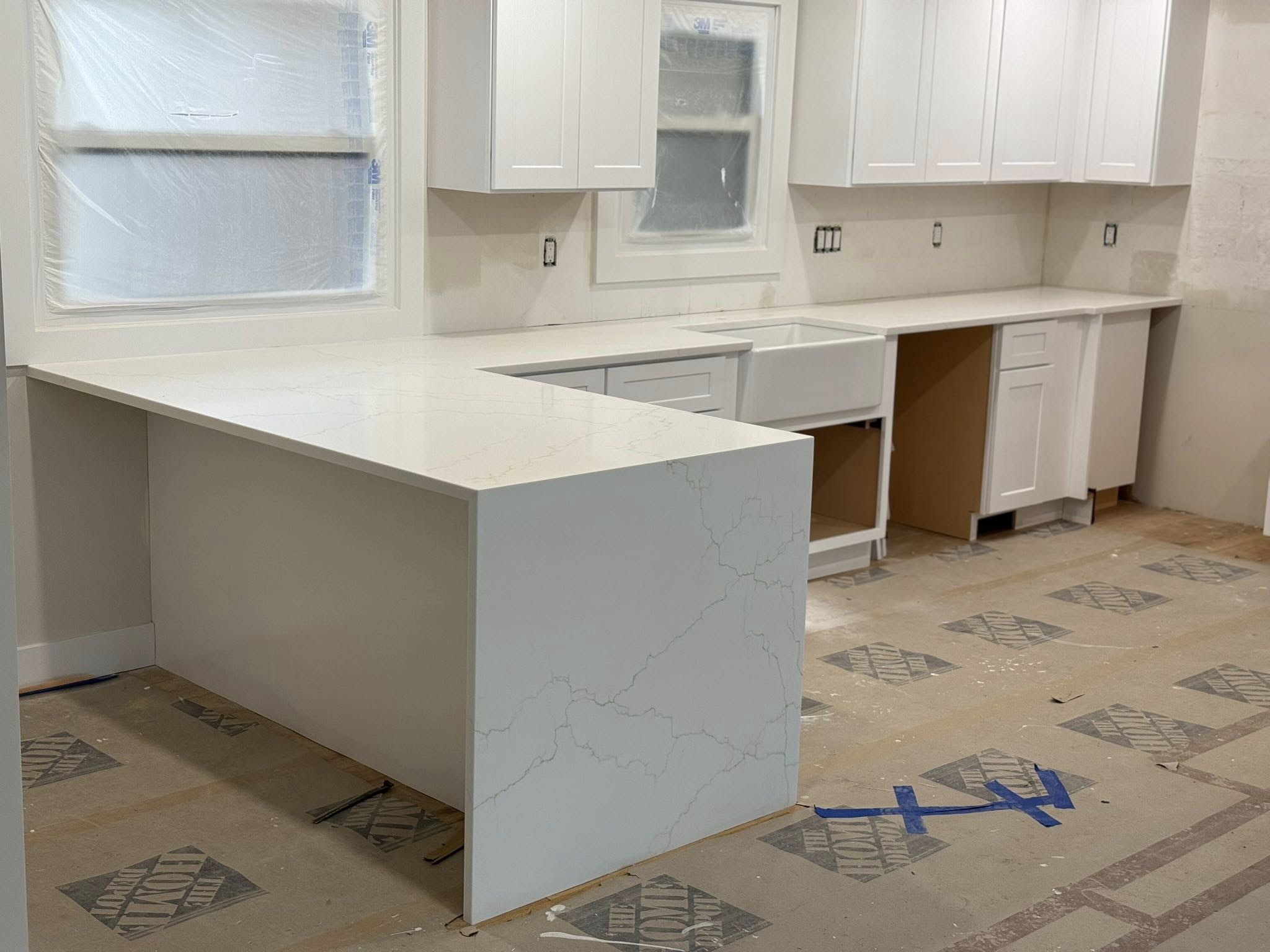 L-shaped white quartz peninsula with a waterfall end in a new-build kitchen with white shaker cabinets and a farmhouse sink