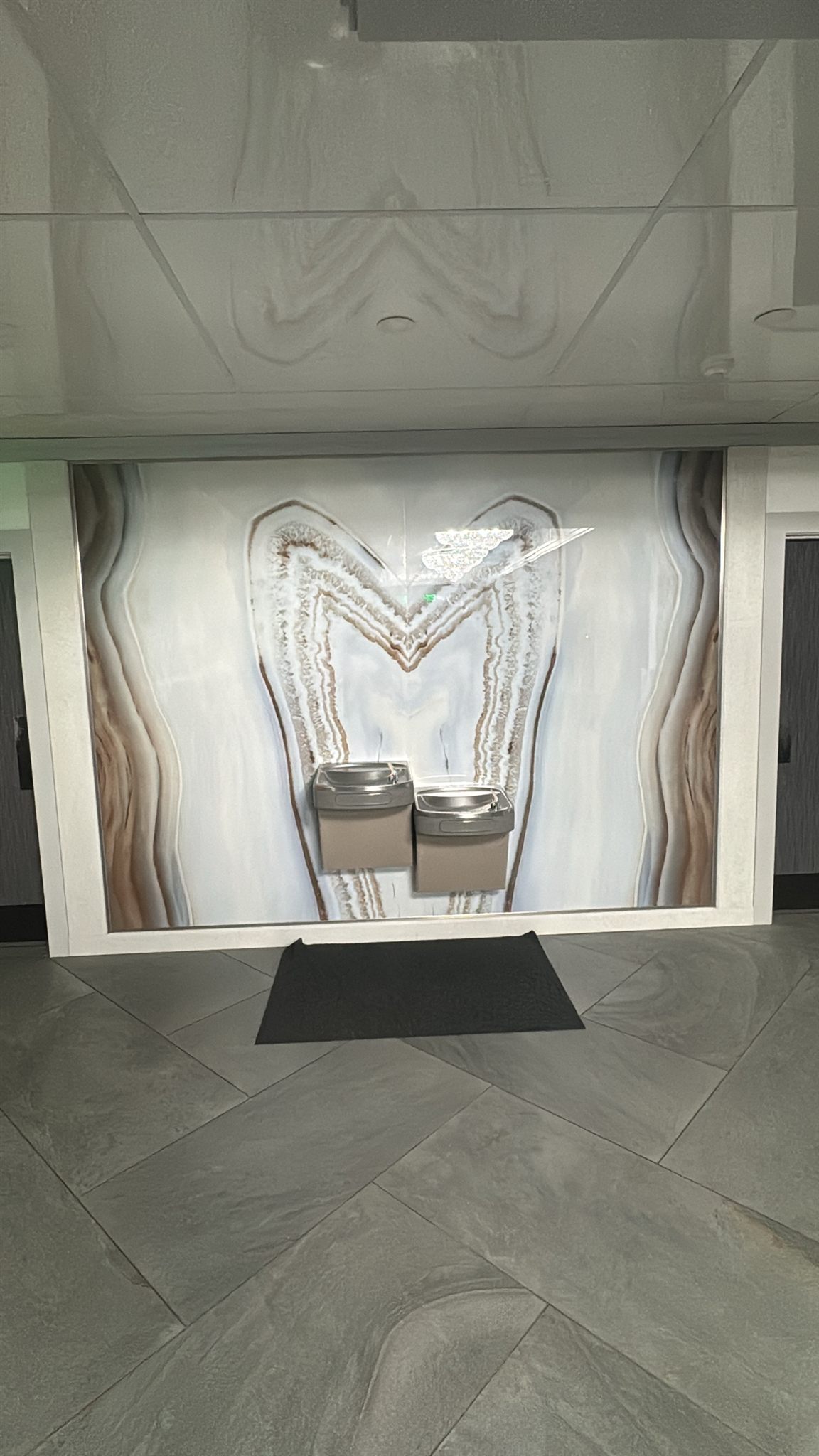 Bookmatched onyx-look slab wall with drinking fountains in a commercial hallway