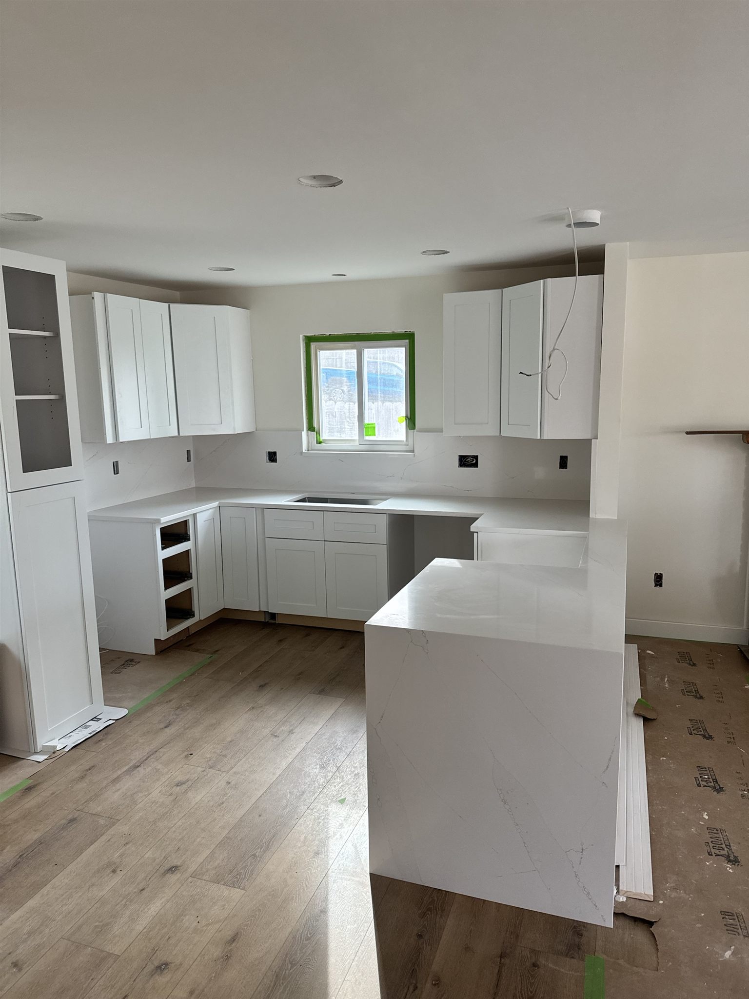 White shaker kitchen with quartz counters, a waterfall peninsula and a full-height quartz backsplash